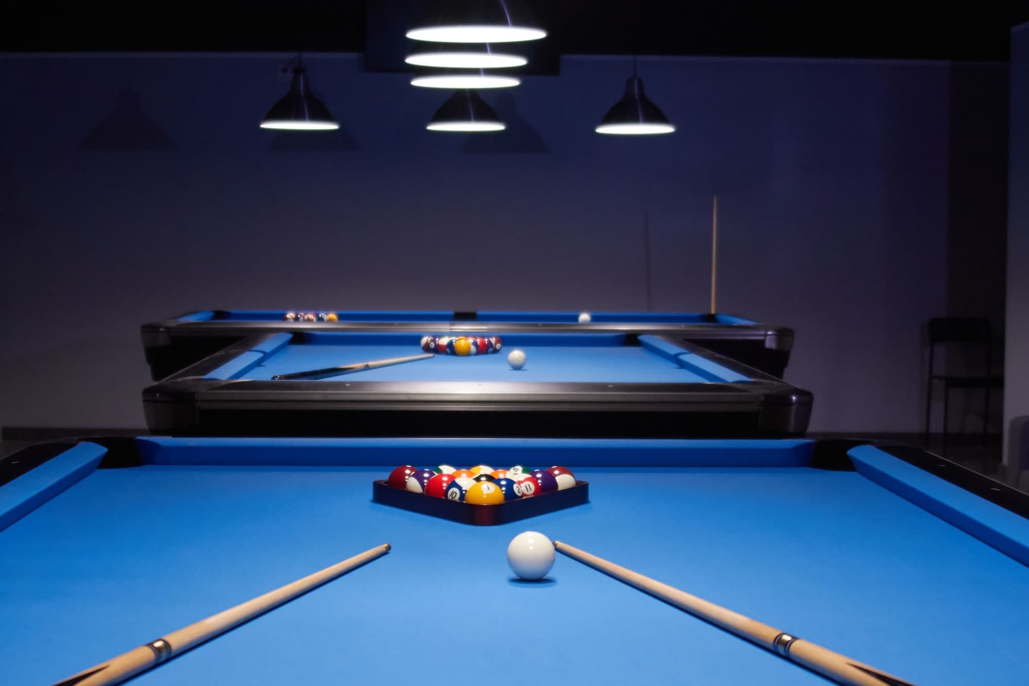 Pool hall with blue tables under pendant lights